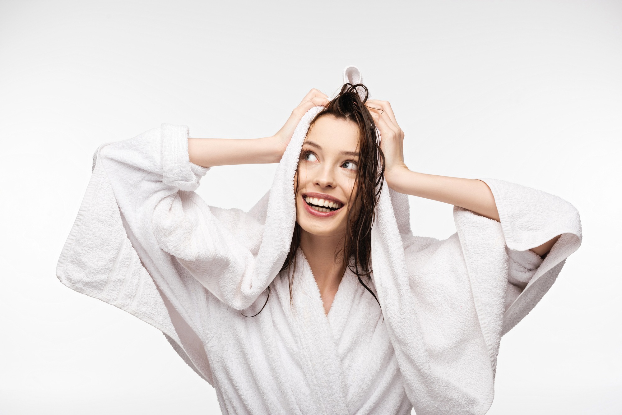 A woman fresh from taking a shower, smiling and drying her hair with a soft towel.