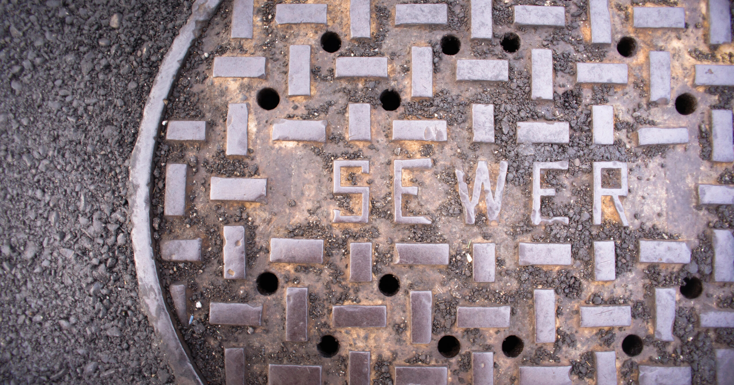 Close-up of a sewer manhole cover set in pavement, marking an underground sewer line
